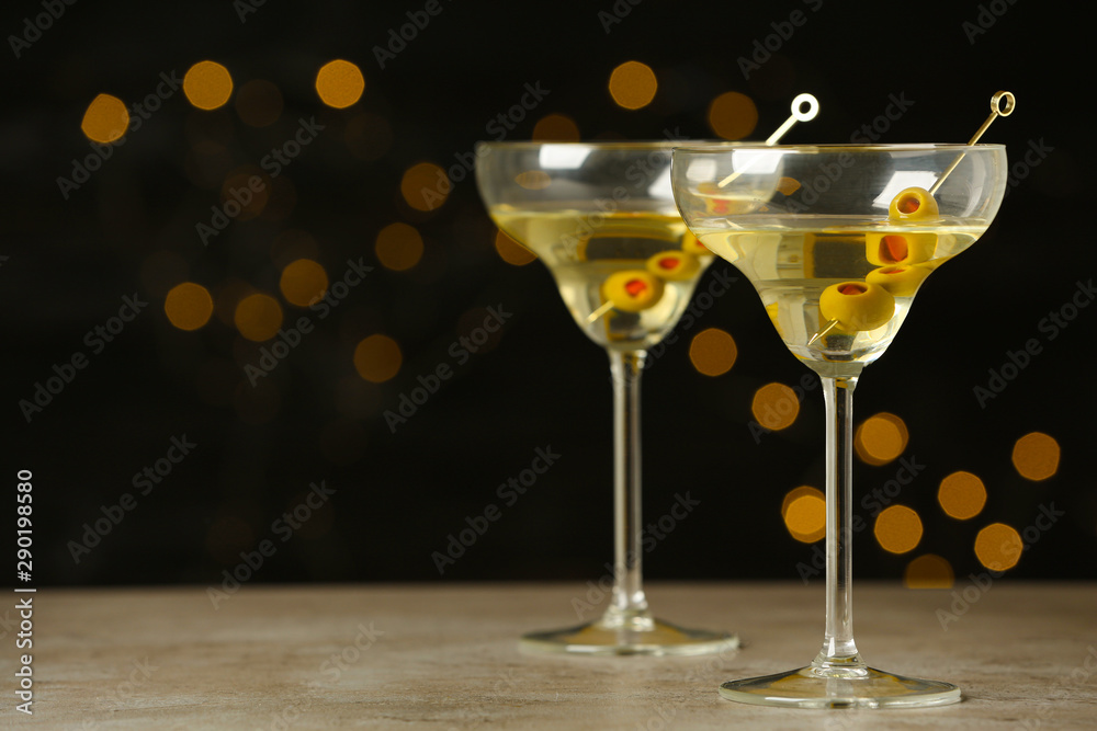 Glasses of Classic Dry Martini with olives on grey table against blurred background. Space for text Glasses of Classic Dry Martini with olives on grey table against blurred background. Space for text