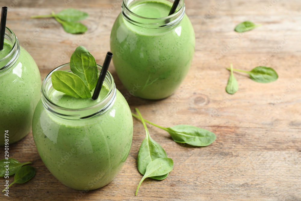 Jars of healthy green smoothie with fresh spinach on wooden table. Space for text Jars of healthy green smoothie with fresh spinach on wooden table. Space for text