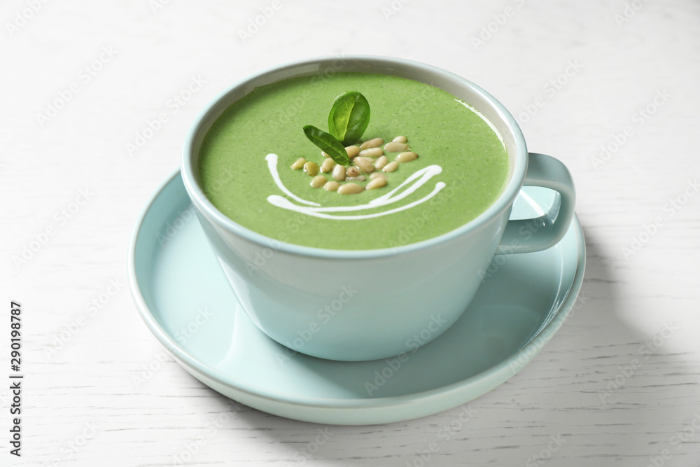 Cup of healthy green soup with fresh spinach on white wooden table