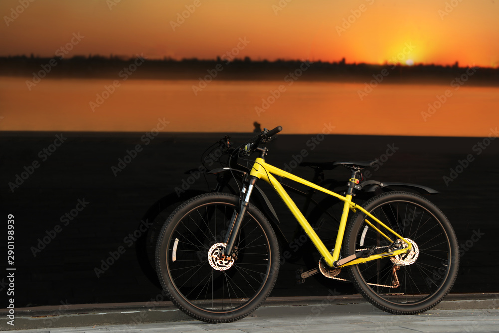 Obraz premium Yellow bicycle parked near glass building at sunset