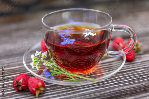 Cup of tea with herbs and fresh berries on a wooden table. Close-up.