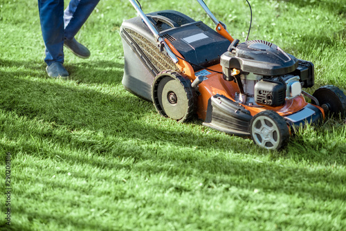 Gardener cutting grass with gasoline lawn mower on the backyard, close-up view