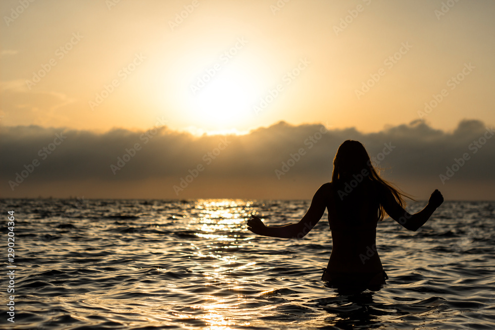 silhouette of young woman in the water at sunset