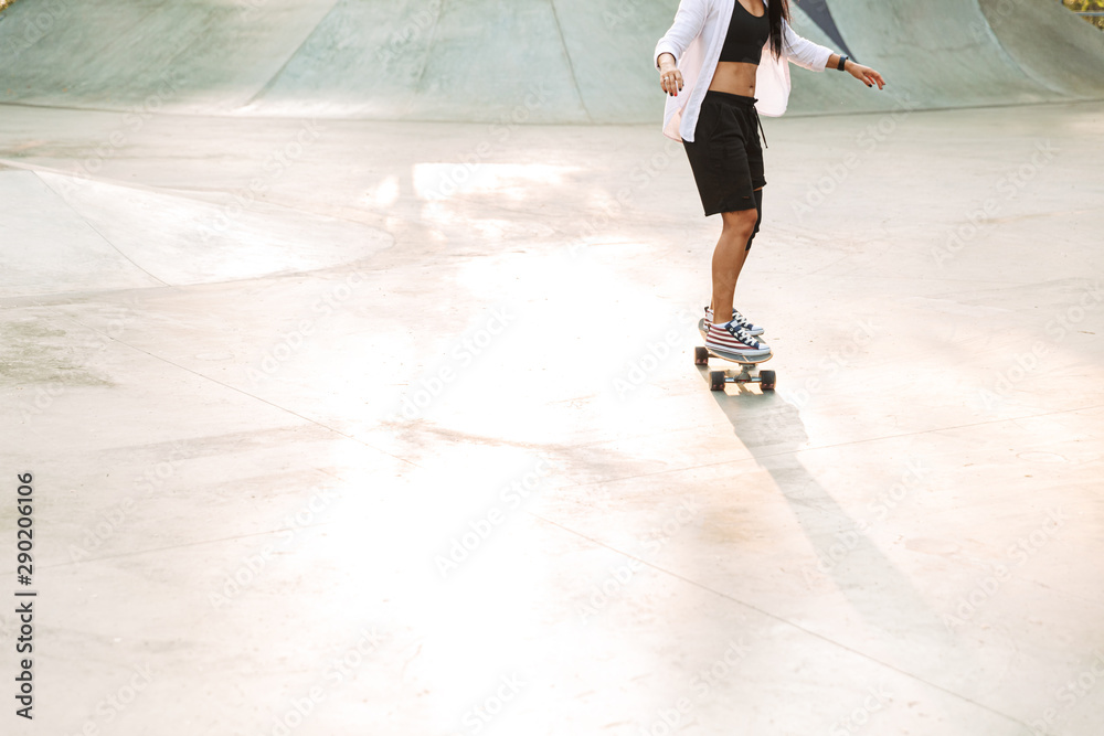 Cropped photo of energetic young woman riding skateboard in skate park