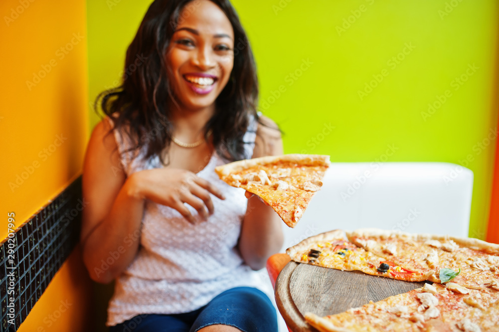 African woman with pizza sitting at bright colored restaurant. African woman with pizza sitting at bright colored restaurant.