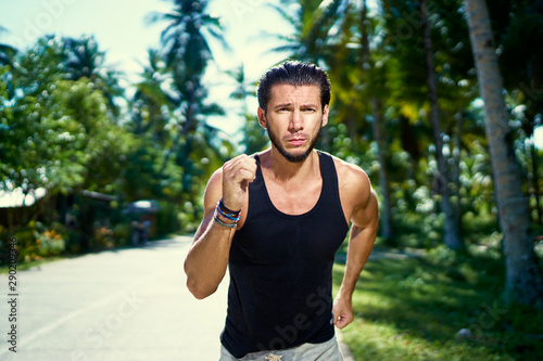Healthy lifestyle. Jogging outdoors. Young strong man is running under palm trees.