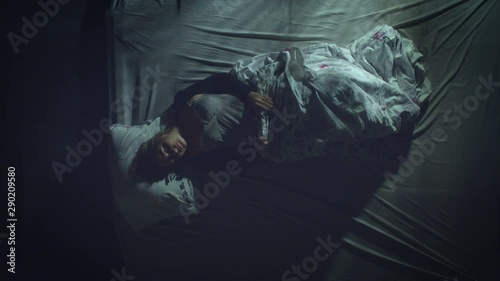 Sleeping woman. Restless sleep.  Top view. A woman sleeps on a bed. She flips from one side to the other.  Light headlamp from passing by the window cars fall on she.