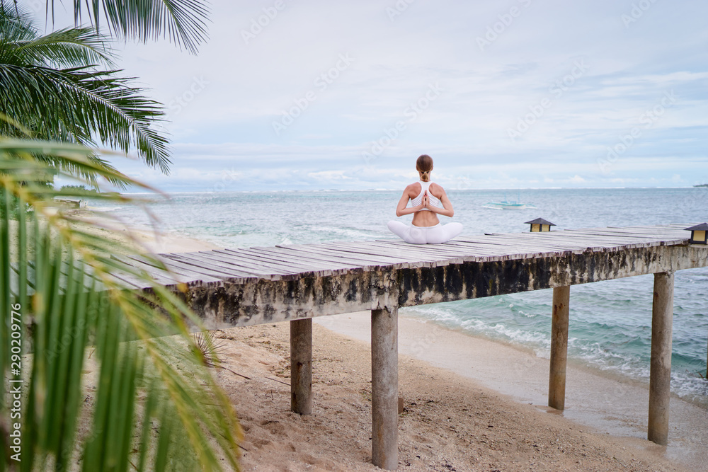 Yoga and meditation. Relaxed young woman in lotus pose on wooden deck with beautiful sea view.