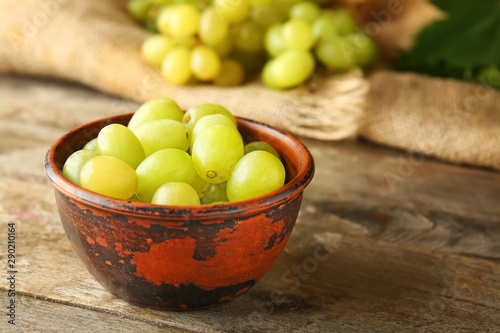 Bowl with sweet grapes on wooden table