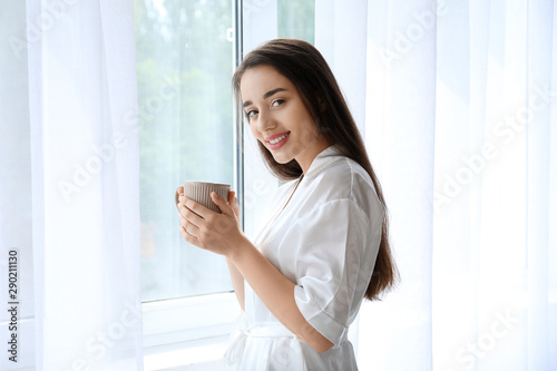 Morning of beautiful young woman drinking coffee near window