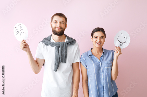 Happy couple holding sheets of paper with drawn emoticons on color background