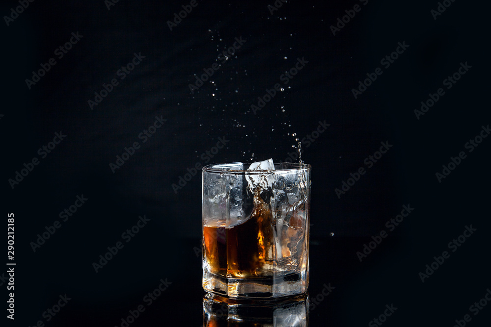 Whiskey splash from the fallen ice cube into glass with beverage isolated on black background.. Whiskey splash from the fallen ice cube into glass with beverage isolated on black background..