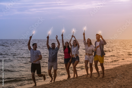 Happy friends with sparklers on sea beach at resort