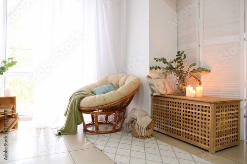 Soft chair with eucalyptus branches and burning candles in interior of room