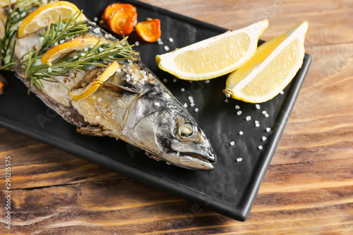 Plate with baked mackerel fish on wooden table