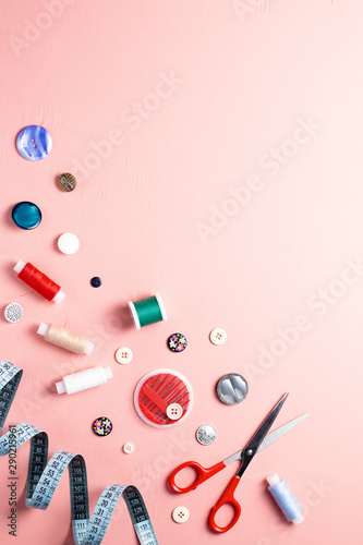 Sewing tools and accessories layout on pink background, top view, copy space
