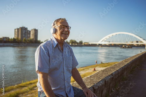 Outdoor portrait of senior man who is listening music on headphones.