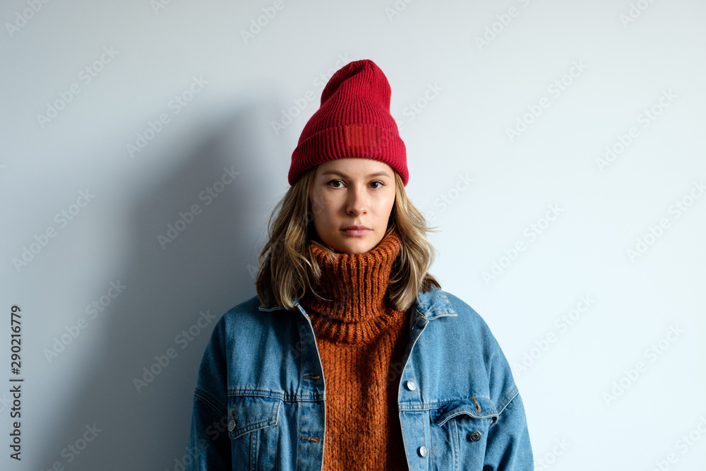 Portrait of a girl in a sweater and a red hat on a white wall background