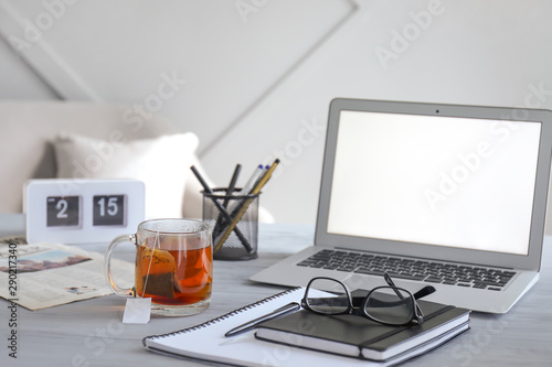 Cup with hot tea, laptop and stationery on table