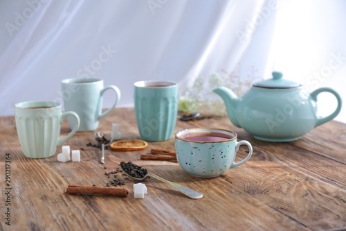 Cups and teapot with hot beverage on wooden table