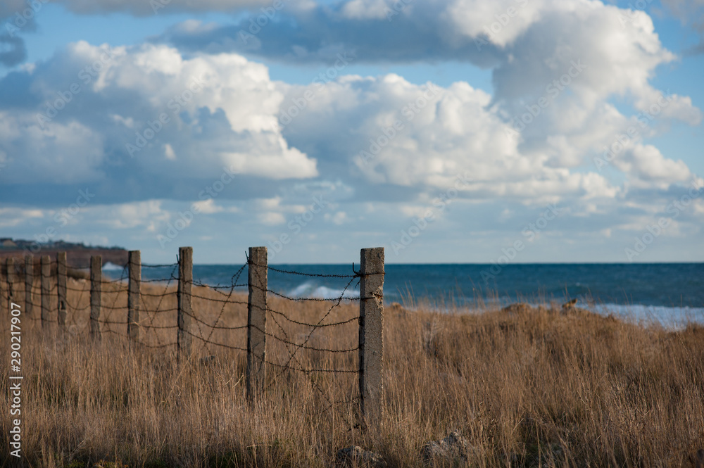 empty place near sea shore with barbed wire fence on border with blue sky and clouds on overcast sunset with copy space