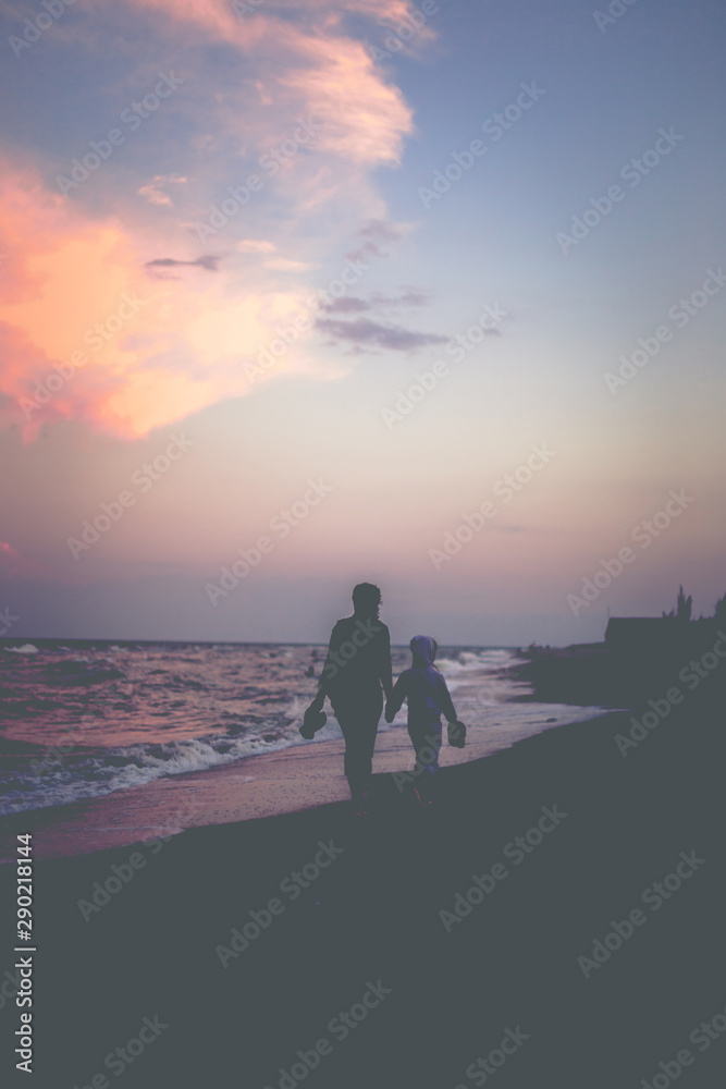 Mother and daughter walk along the beach at sunset