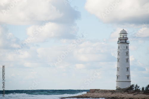 overcast weather concept white lighthouse on edge of the world near stormy sea with waves on cloudy sky backdrop with copy space