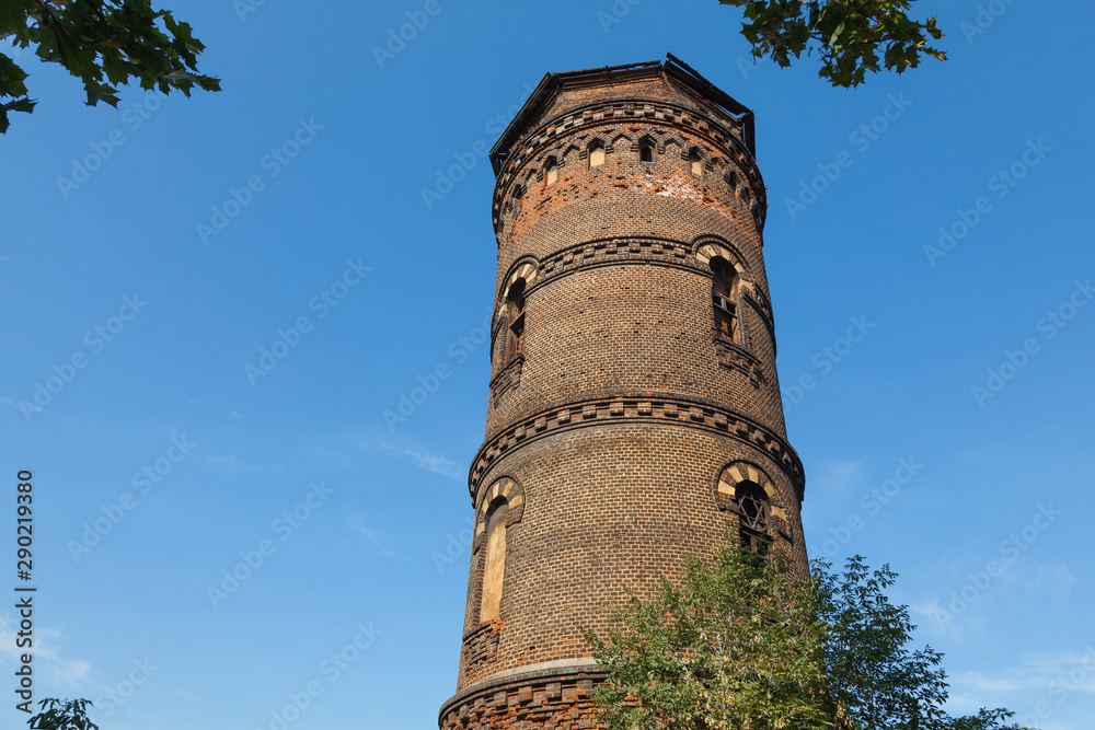 Old red brick water tower with windows of different sizes against a blue sky