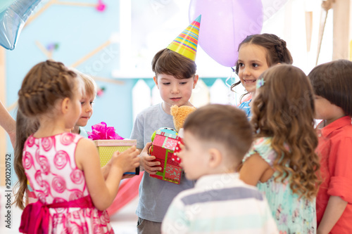holidays, childhood and celebration concept - group of happy friends kids greeting and giving presents to birthday child at party in daycare