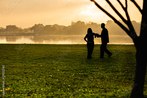 Silhouette of senior couple doing Tai Chi exercise in the park at sunrise. © bignai