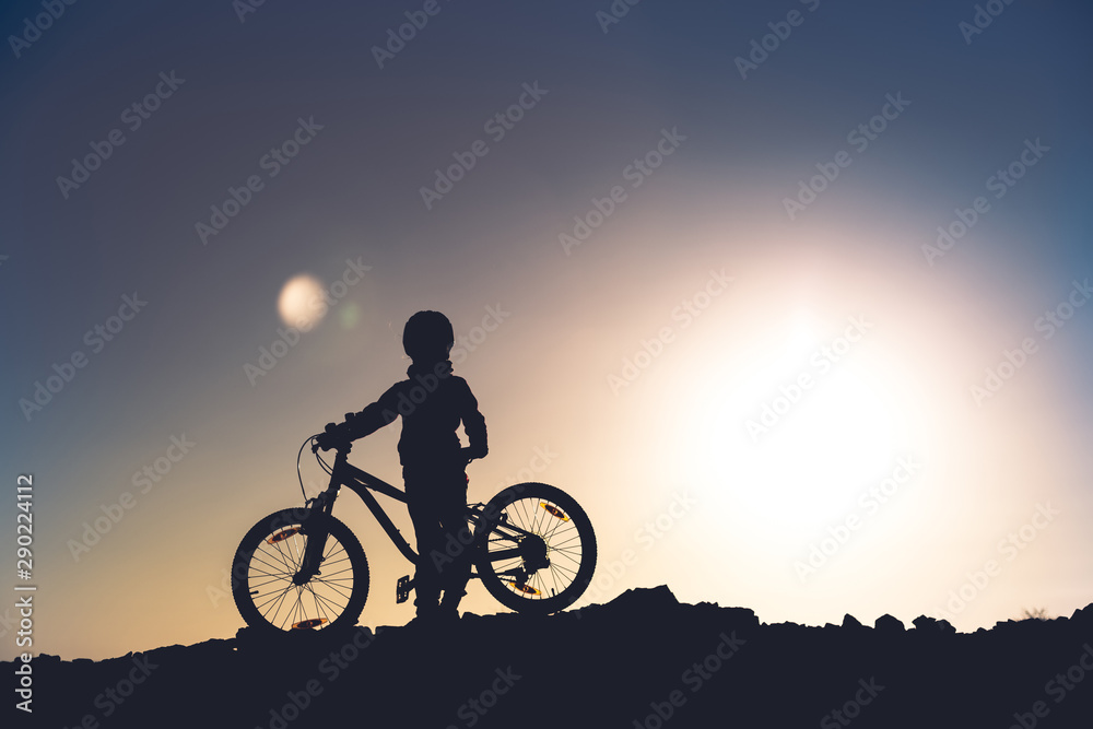 Silhouette of a little girl with a bicycle at sunset