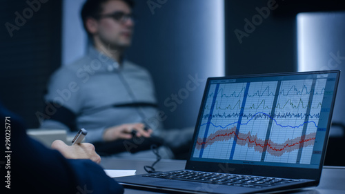 Computer Shows Physiological Measures of a Man Undergoing Lie Detector / Polygraph Test. Examining Expert Writes Down Observations.  photo