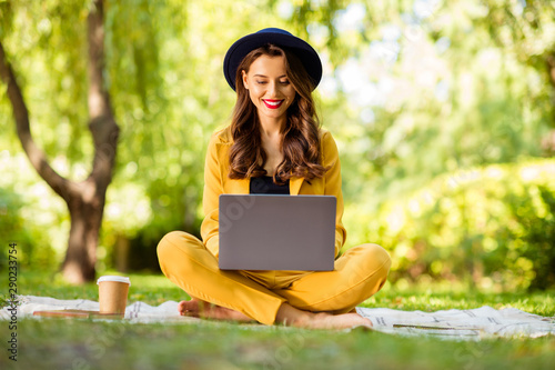 Portrait of her she nice-looking attractive lovely charming winsome trendy pretty cheerful cheery wavy-haired girl sitting in lotus pose typing on laptop in green park outdoors photo