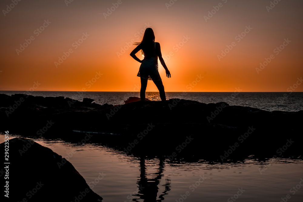 Lifestyle, a young blonde on her back in a red sunset at the ocean with a relaxed gesture