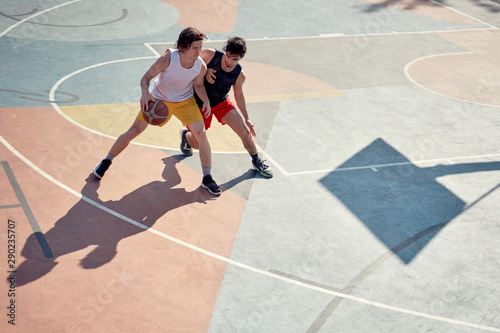Top view photo of two athletes men playing basketball on playground in morning. © Sergey