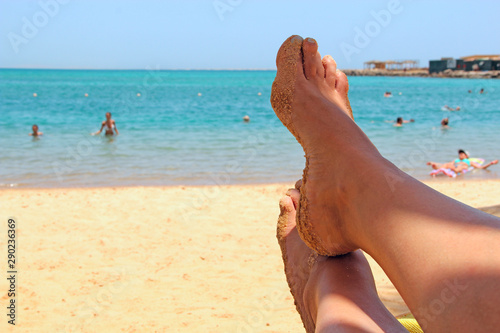 Legs covered by sand of girl sunbathing under sunshade. Enjoying summer vacations