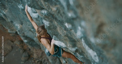 Cinematic slow motion rock climbing moment - strong fit woman makes a big reaching move on over hanging rock wall