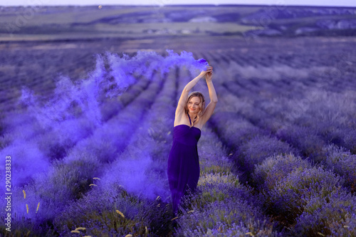 Fototapeta Naklejka Na Ścianę i Meble -  Beautiful girl on the lavender field with colored smoke Beautiful woman in the lavender field on sunsete