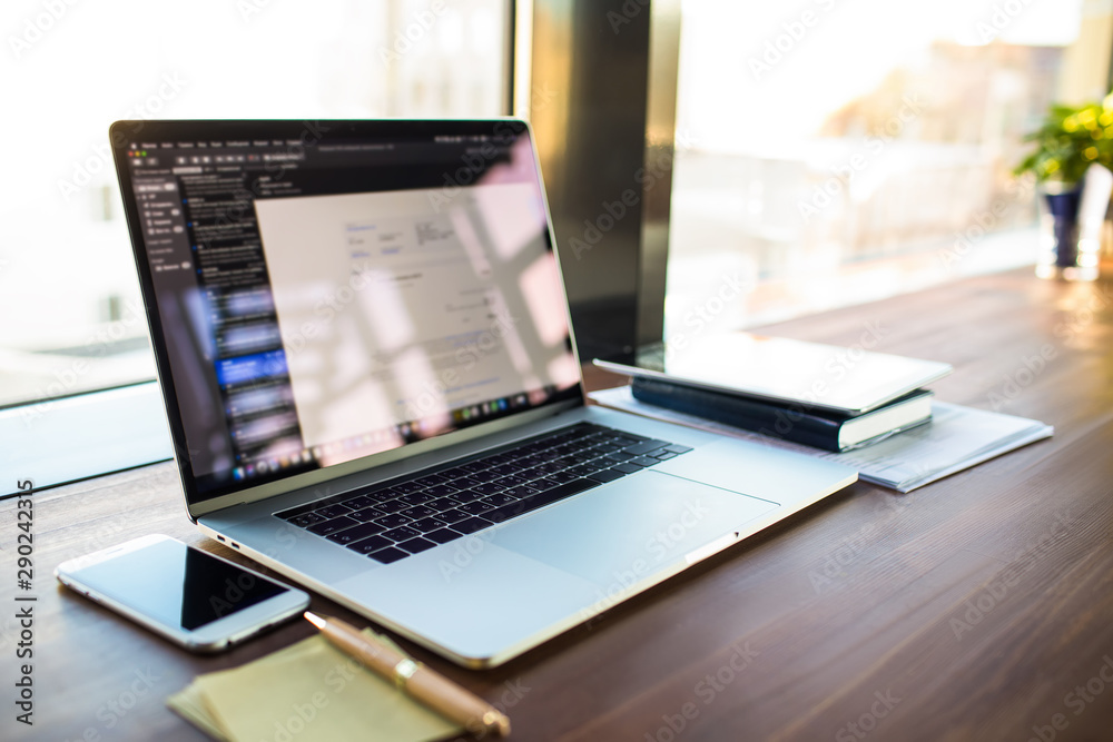 Fototapeta premium Workplace with open pc laptop computer lying on a desktop near working tools in coworking space. Workstation with modern netbook device, mobile phone and touch pad in office interior.