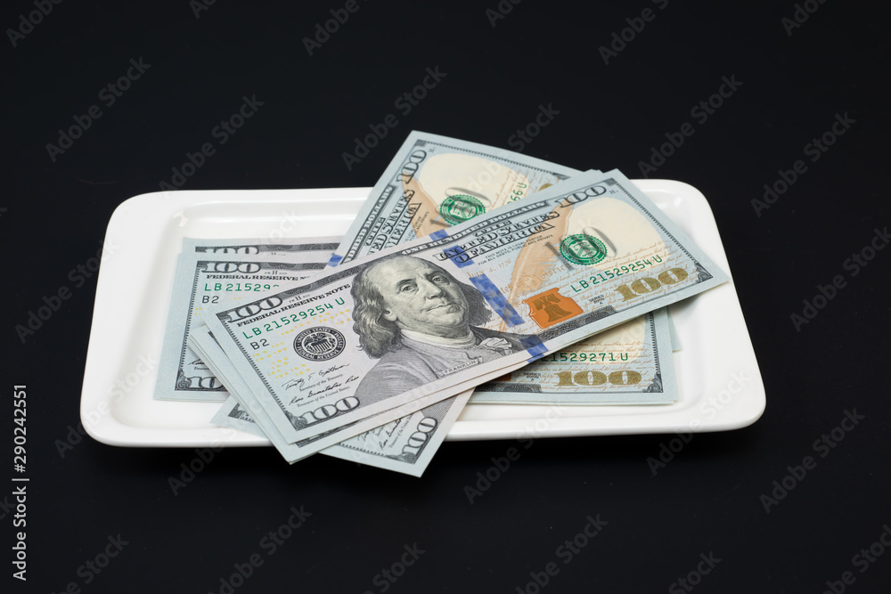 a pack of hundred-dollar bills on a white plate on a black background a pack of hundred-dollar bills on a white plate on a black background