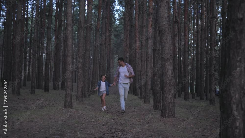 family enjoys weekend in the forest, merry father with daughter holding hands running between the rows of pines at evening in slow motion family enjoys weekend in the forest, merry father with daughter holding hands running between the rows of pines at evening in slow motion