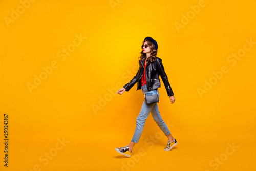 Full length profile side photo of focused gorgeous girl walk on stroll wear black leather jacket denim jeans isolated over yellow color background