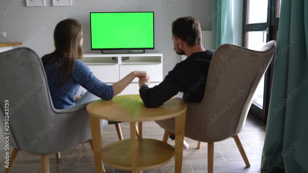 Man and woman are sitting in chairs, kissing and watching TV with a ...