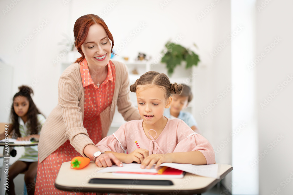 Smiling teacher helping girl with writing down letters Smiling teacher helping girl with writing down letters