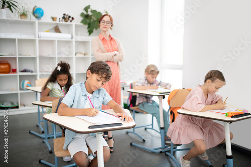 Teacher wearing glasses watching children writing test