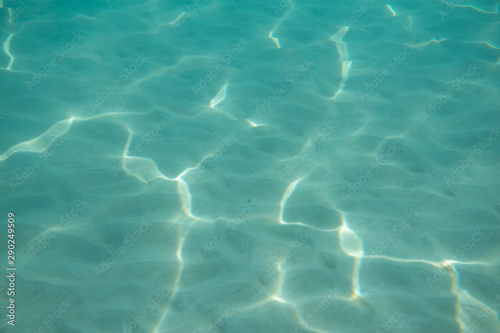 Underwater. Sun glare at the bottom of the sea. Waves underwater and rays of sunlight shining through. Deep turquoise blue sea. Ocean. Transparent water and light at sand.