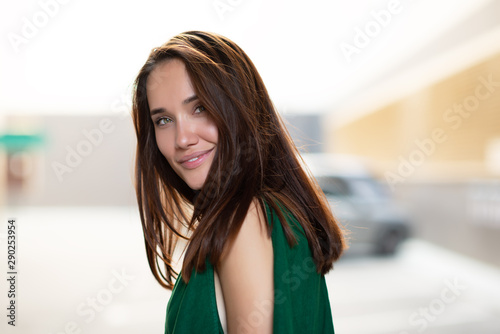 Young pretty likable cheerful woman posing summer city outdoor. Beautiful self-confident girl dressed in emerald-colored jumpsuit with long brown hair walking street enjoing her life, urban lifestyle