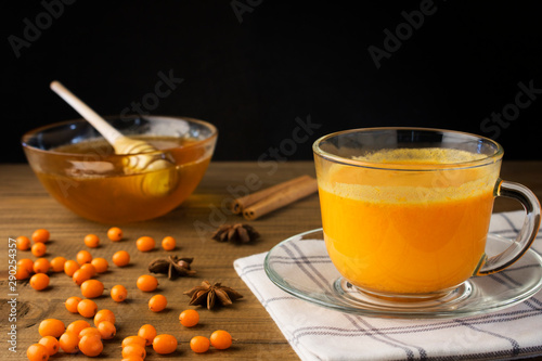 Tea of sea-buckthorn berries on dark wooden background. Vitaminic healthy sea buckthorn tea with fresh raw sea buckthorn berries, with honey and cinnamon sticks, horizontal view. photo