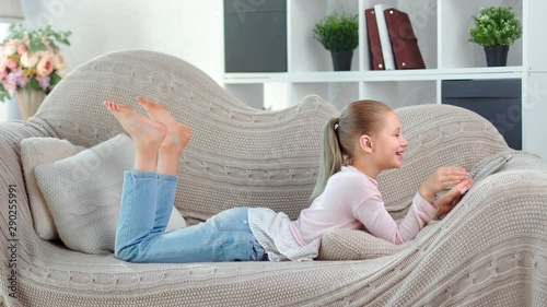 Adorable barefoot domestic child girl laughing having fun looking at screen of tablet pc