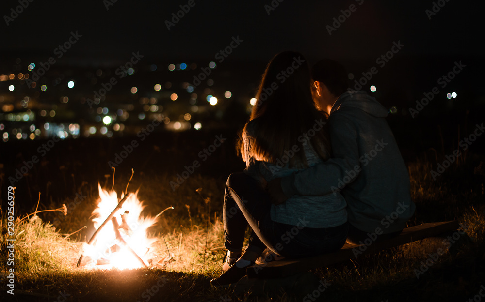 loving couple at night near the fire. couple watching the city at night. beautiful night vision scenery. campfire around people, be near the fire, the concept of relaxation loving couple at night near the fire. couple watching the city at night. beautiful night vision scenery. campfire around people, be near the fire, the concept of relaxation